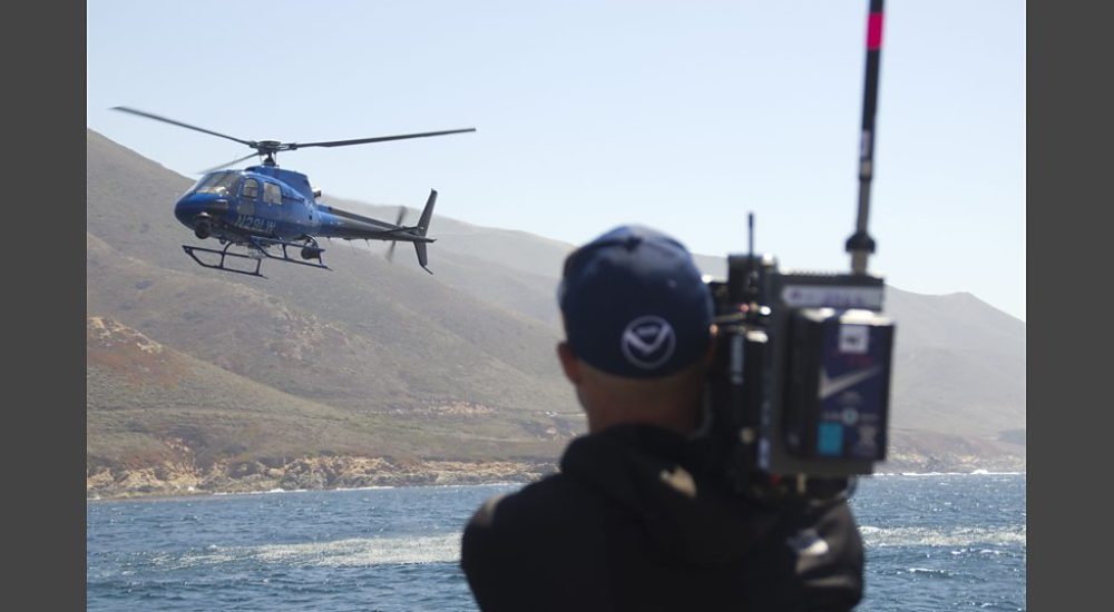 Helicopter over ocean with video camera operator in foreground